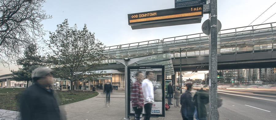 People waiting for the bus next to a bus stop with a BPIDs display