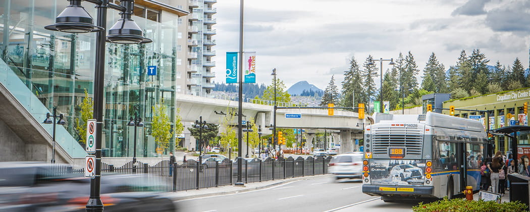 A bus parked at a bus bay in front of a SkyTrain station on a bright and sunny day