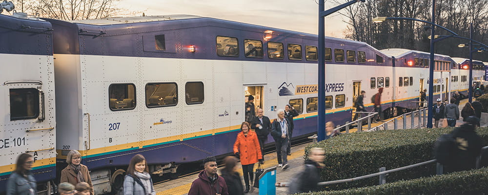 A long passenger train stopped at a station and passengers embarking off and walking up stairs to ground level