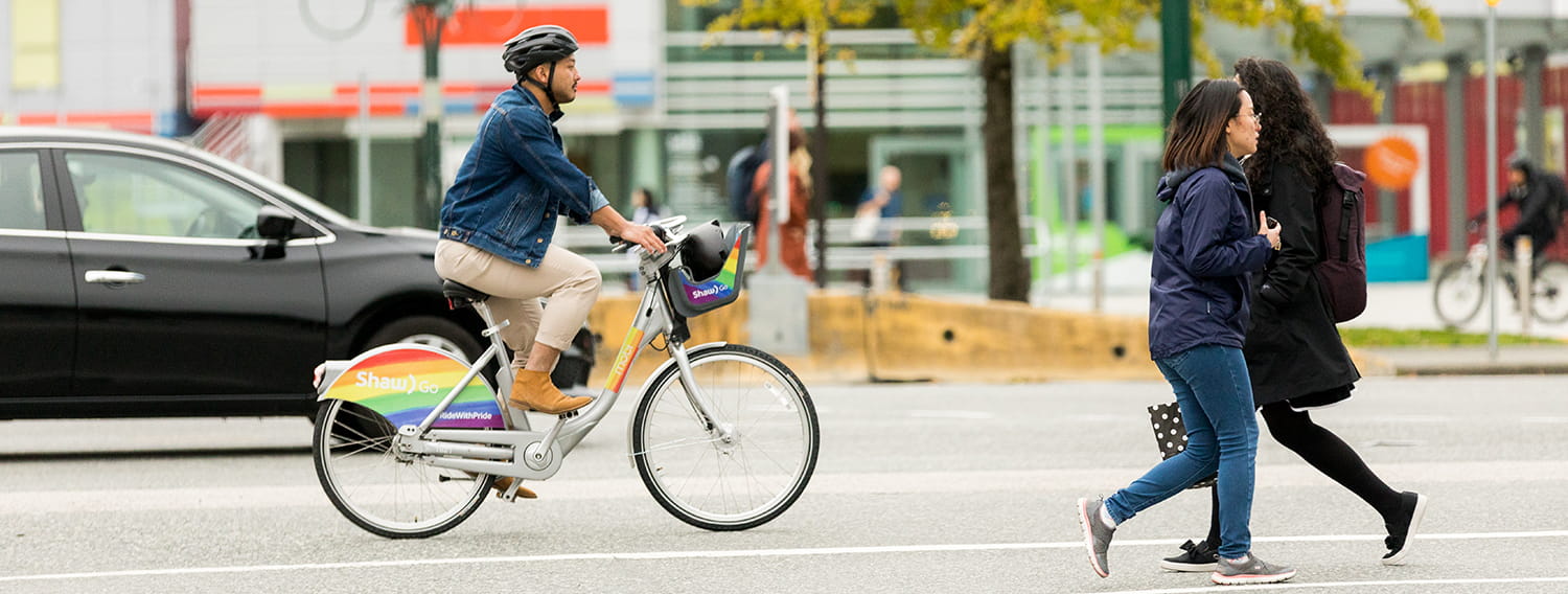 A man biking down the street with pedestrians and cars passing by